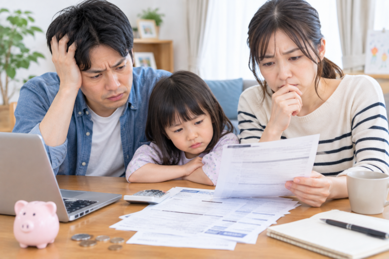 請求書やパソコンを前に家計について悩む夫婦と子ども