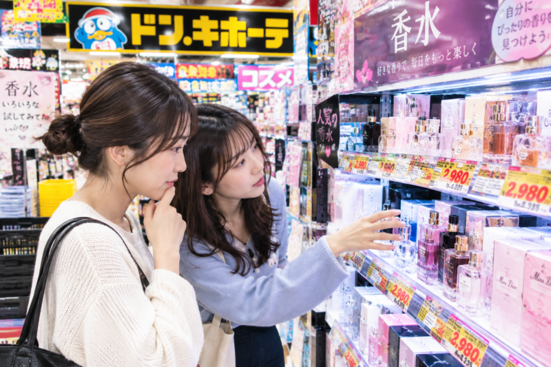 ドン・キホーテのコスメ棚前で展示されている香水を手にとり選ぶ2人の女性